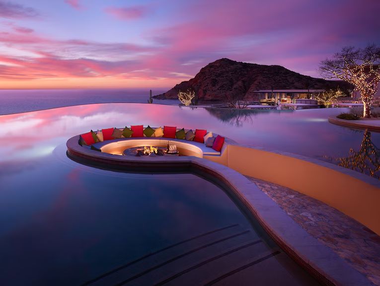 Infinity pool with sunken firepit lounge overlooking the sea at sunset